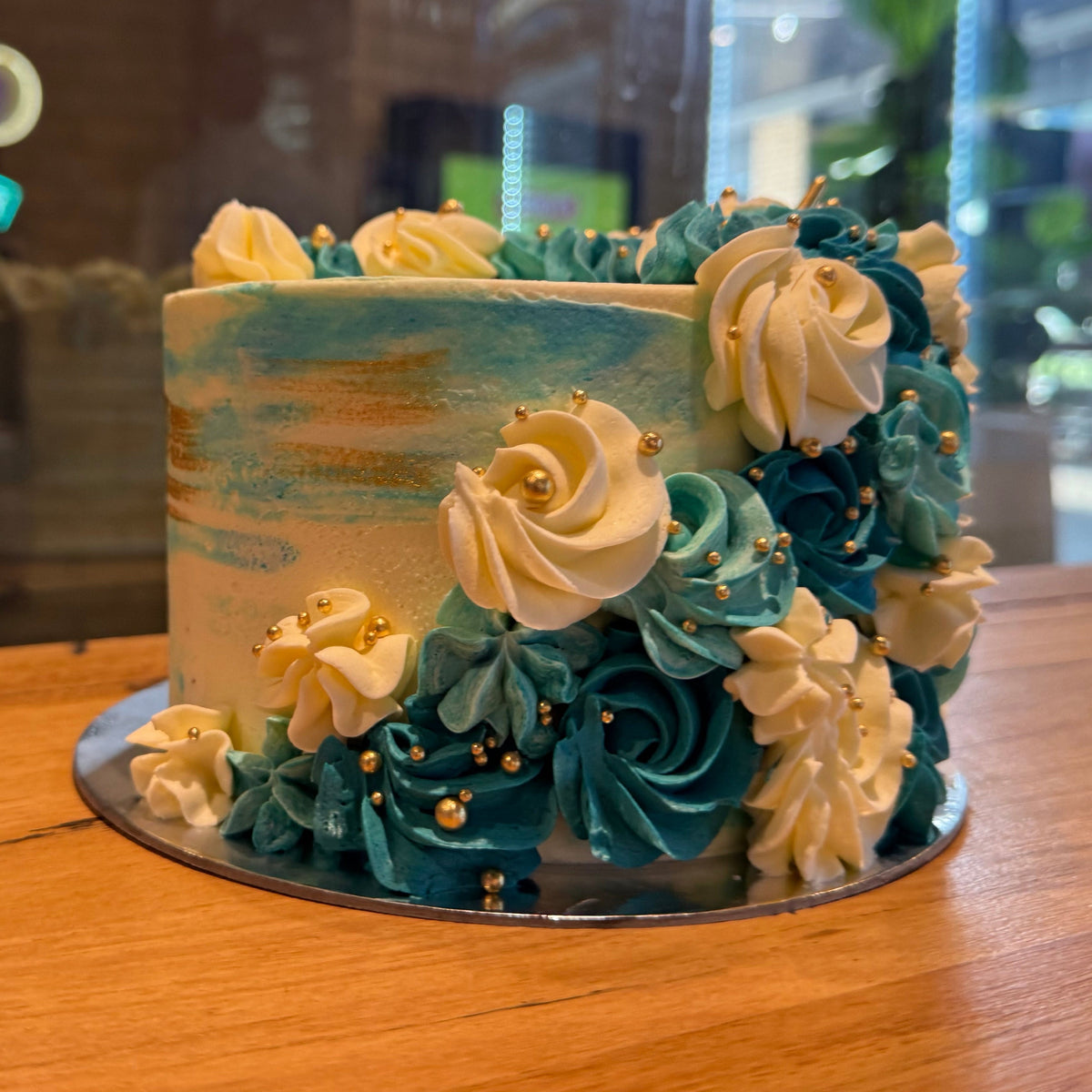 Front view of a blue, white and gold celebration cake in Adelaide, showcasing its flowing decorative design and elegant gold accents.