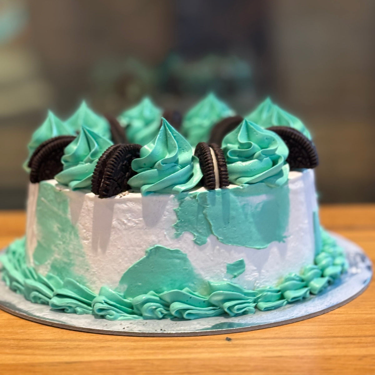 front view of a handcrafted Oreo drip ice cream cake highlighting the colourful green and aqua finish and flowing decorative drips.