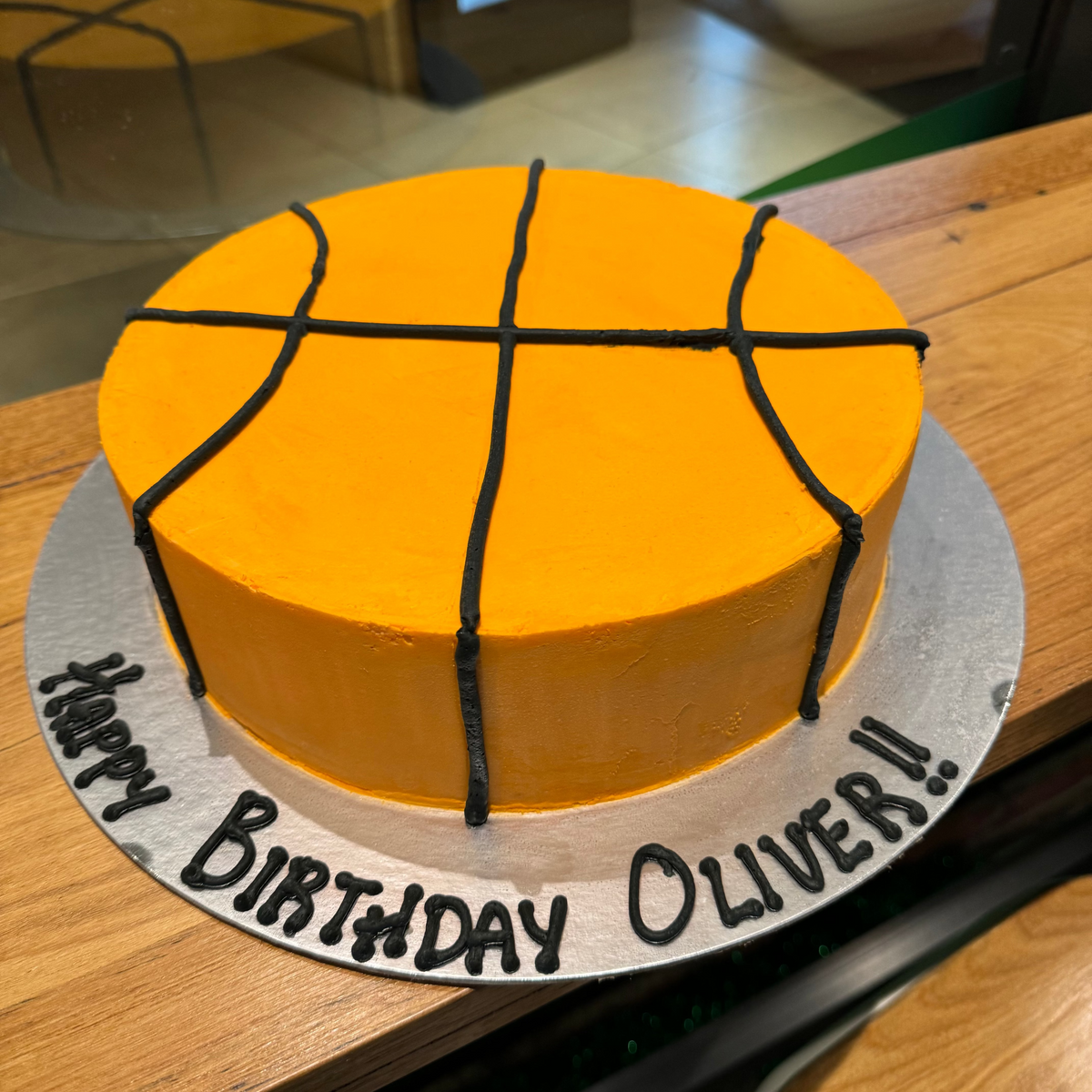 Full view of a round basketball birthday ice cream cake with a classic basketball-inspired design and smooth finish without decorative piping.