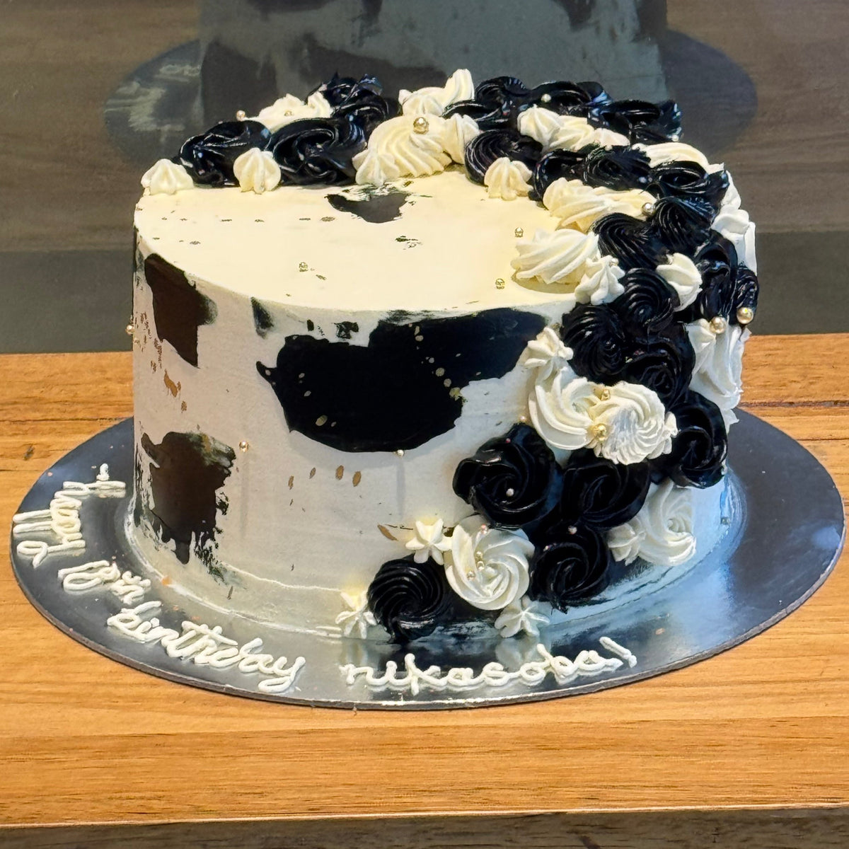 Full view of a black, gold and white cascading mud or sponge cake handcrafted in Adelaide, featuring elegant flowing decorations and gold accents.