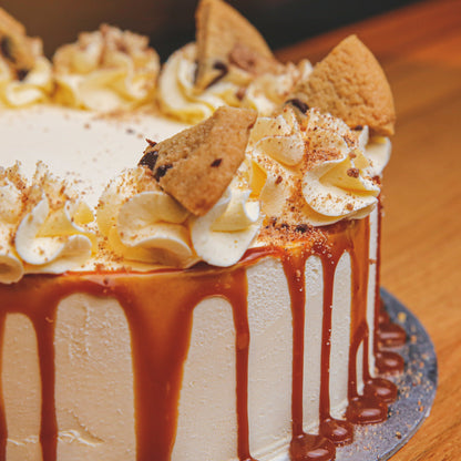 Side view of a choc chip cookie ice cream cake highlighting the caramel drip running down the cake and its dessert-inspired decorations.