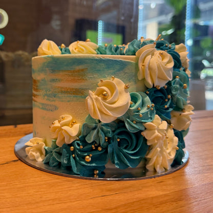 Front view of a blue, white and gold celebration cake in Adelaide, showcasing its flowing decorative design and elegant gold accents.