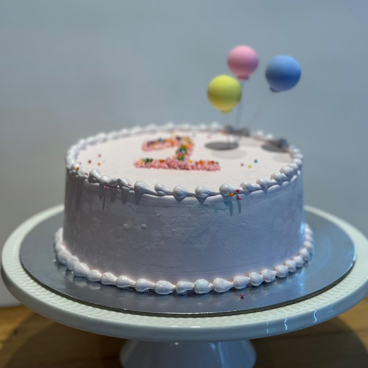 front view of a handcrafted first birthday cake featuring festive balloon decorations, made in Adelaide with Ben & Jerry's ice cream.
