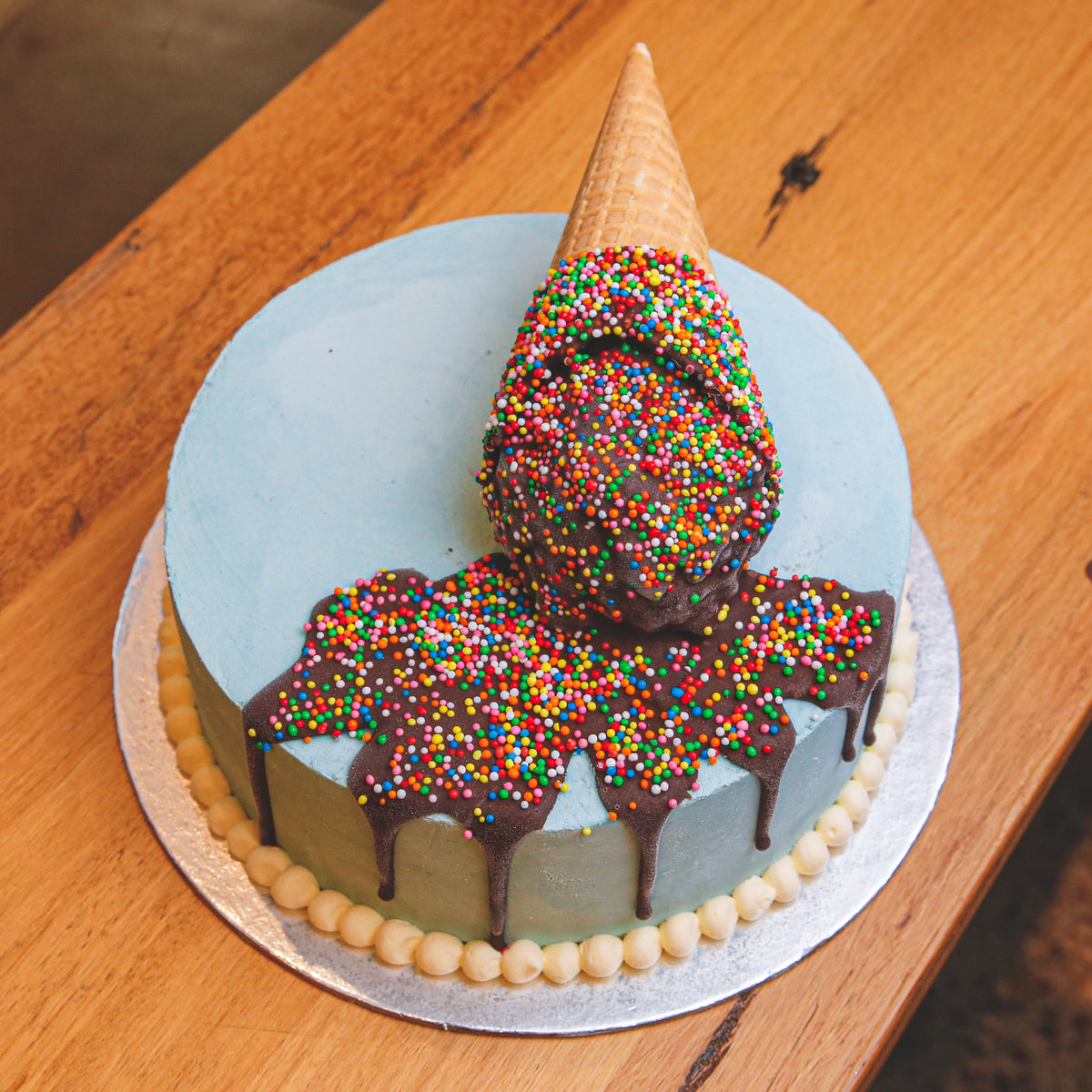 Full view of a melting ice cream cone birthday cake featuring a playful cone topper and melting scoop-inspired design for celebrations.