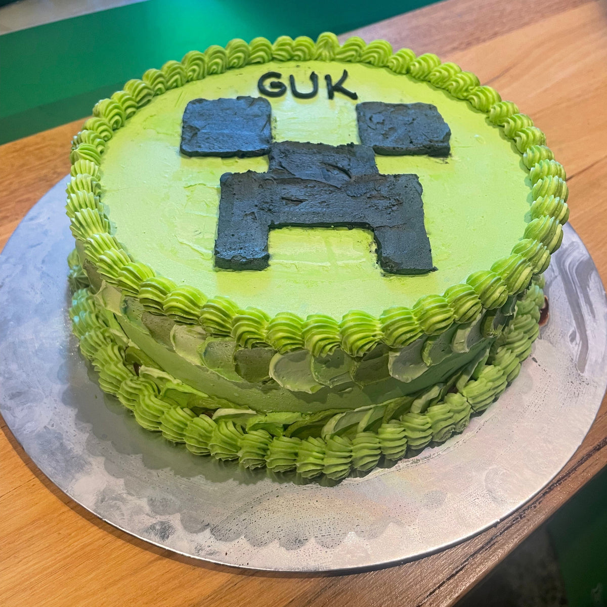 front view of a handcrafted Minecraft birthday cake highlighting its green Creeper-inspired finish and pixelated gaming details.