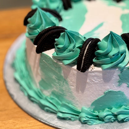 close up of an Oreo birthday ice cream cake showcasing its vibrant green and aqua colour scheme, decorative drip finish, and cookie accents.