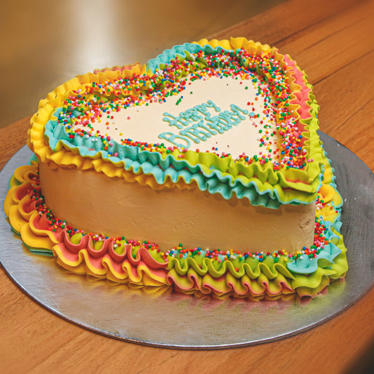 side view of a handcrafted rainbow heart ice cream cake showcasing its vibrant colour theme and playful birthday decorations.