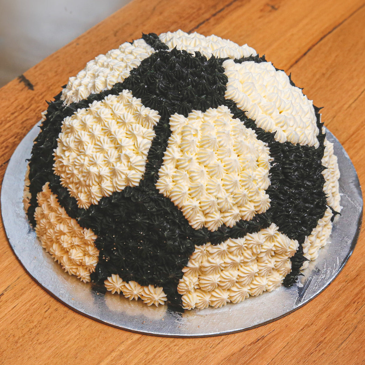 Full view of a 3D dome-shaped soccer ball ice cream cake featuring a classic black-and-white football pattern for a sports-themed birthday.