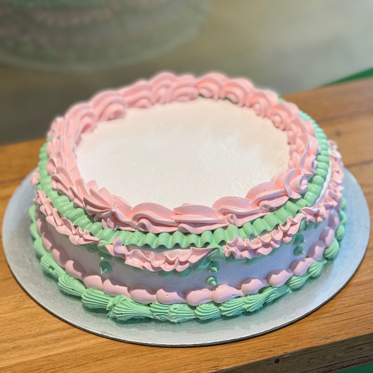 Full view of a vintage white and baby pink birthday cake handcrafted in Adelaide using Ben & Jerry's ice cream, featuring delicate pastel piping.