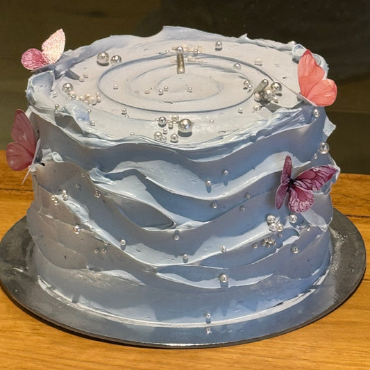 Full view of a baby blue and white wave-effect mud or sponge cake in Adelaide, featuring elegant flowing decorations for birthdays and baby showers.