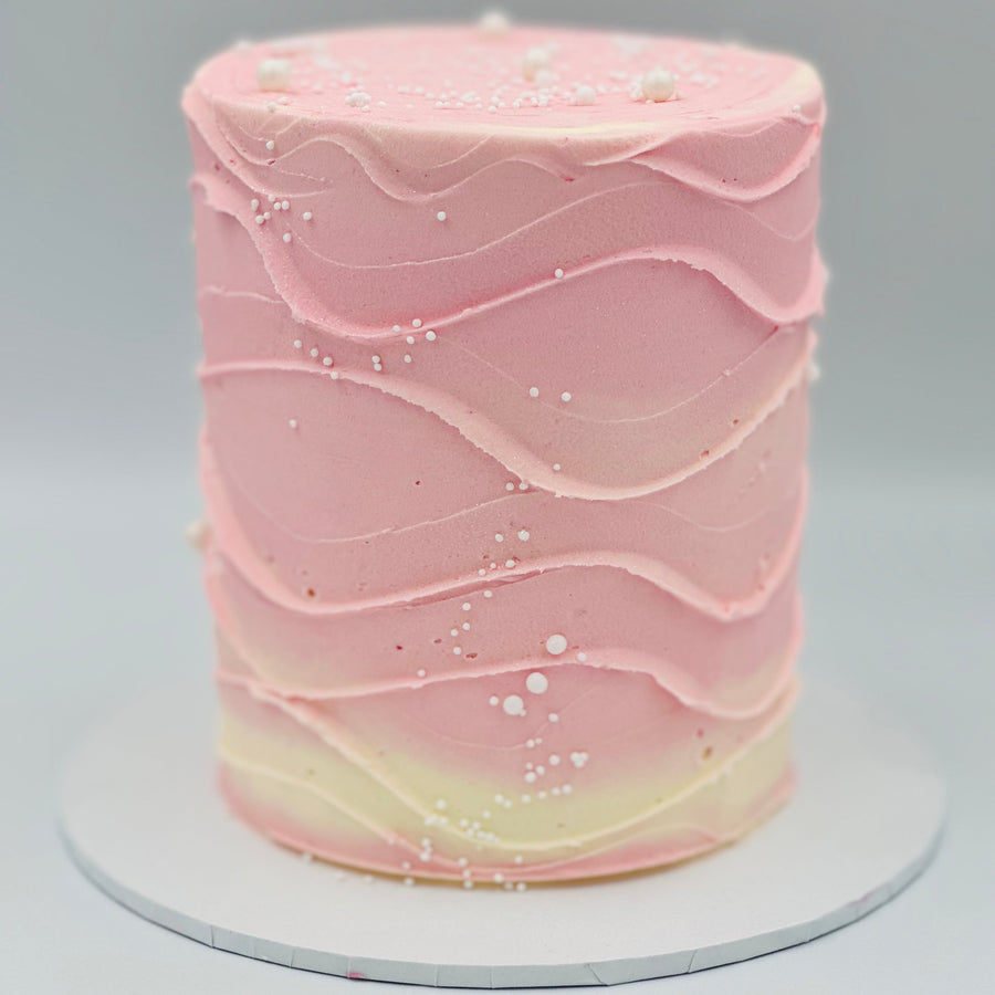 Full view of a baby pink and white wave-effect mud or sponge cake in Adelaide, featuring soft pastel colours and flowing decorative details.
